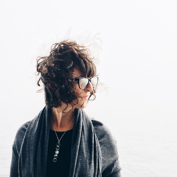 Person with curly hair wearing glasses and a gray scarf on a white background