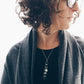 Person wearing a dark gray scarf and a necklace with a pendant, against a neutral background