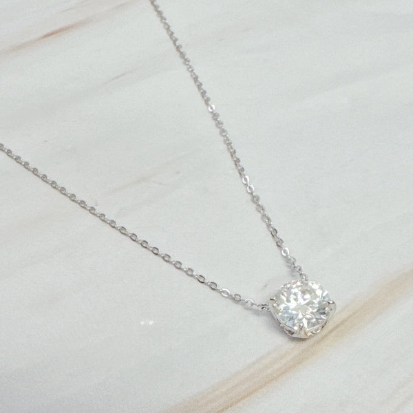 Silver necklace with a round diamond pendant on a light wooden surface