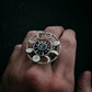 Hand wearing a silver ring with a blue gemstone against a dark background