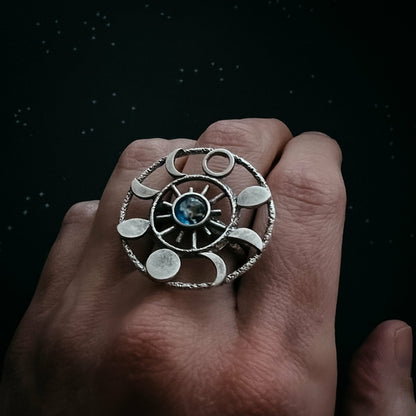 Hand wearing a silver ring with a blue gemstone against a dark background