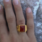 Gold ring with a red stone on a person's finger against a textured background