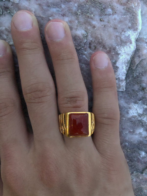 Gold ring with a red stone on a person's finger against a textured background