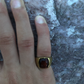Hand wearing a gold ring with a red stone on a textured surface