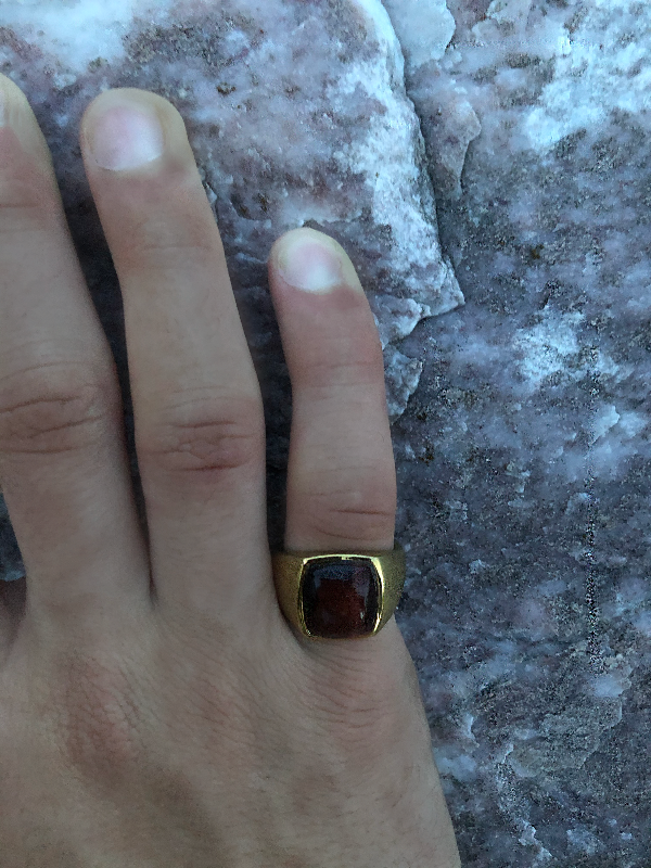 Hand wearing a gold ring with a red stone on a textured surface