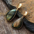 Gold-framed labradorite earrings on a stone surface