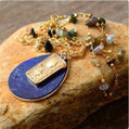 Gold necklace with a blue pendant on a stone surface