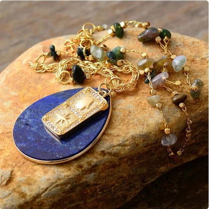 Gold necklace with a blue pendant on a stone surface