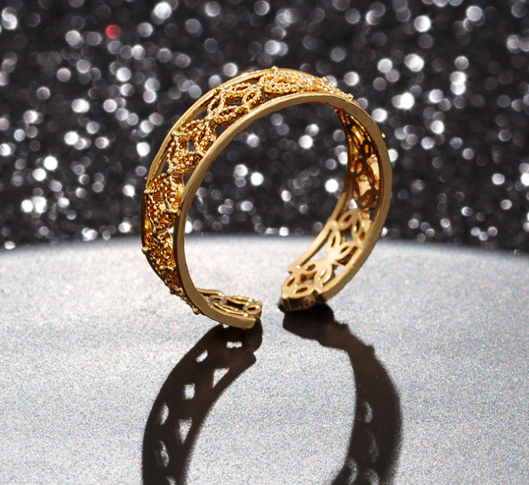 Gold bracelet with intricate design on a reflective surface with a glittery background