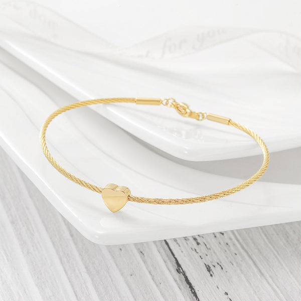 Gold bracelet with a heart charm on a white surface