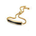 Gold bracelet with a black bar clasp on a white background