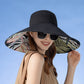 Woman wearing a large black sun hat with a colorful interior against a clear blue sky.