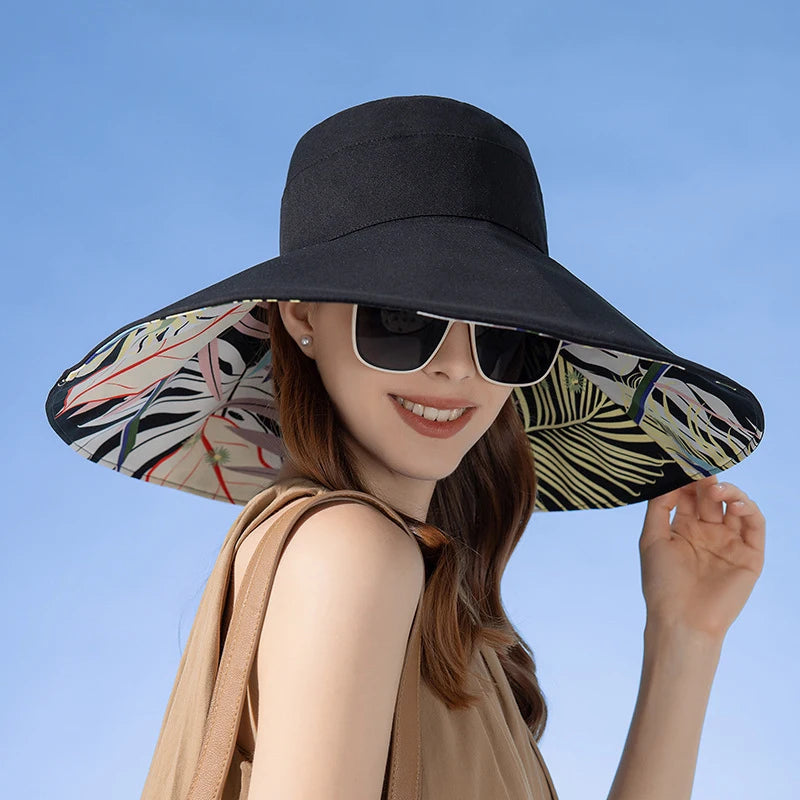 Woman wearing a large black sun hat with a colorful interior against a clear blue sky.