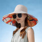 Woman wearing a large sun hat with a colorful brim against a clear blue sky