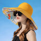 Woman wearing a yellow sun hat with a colorful floral interior against a clear blue sky.