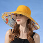 Mannequin wearing a yellow sun hat with a colorful floral interior against a blue sky.
