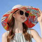 Woman wearing a colorful sun hat and sunglasses against a clear blue sky