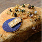 Gold necklace with blue pendant on a stone surface