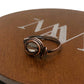 Bronze ring with a clear gemstone on a brown leather surface with a brand logo.