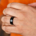 Close-up of a hand wearing a black ring with an orange background