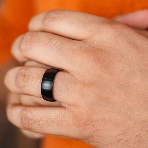 Close-up of a hand wearing a black ring with an orange background