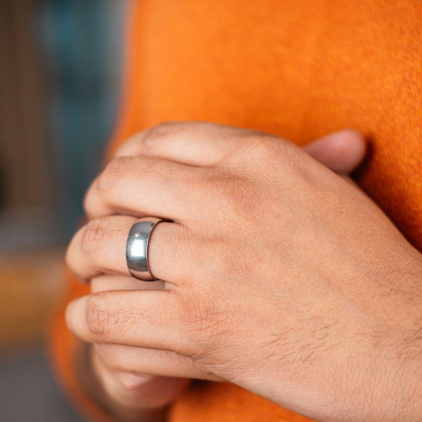 Hand wearing a silver ring with an orange garment in the background