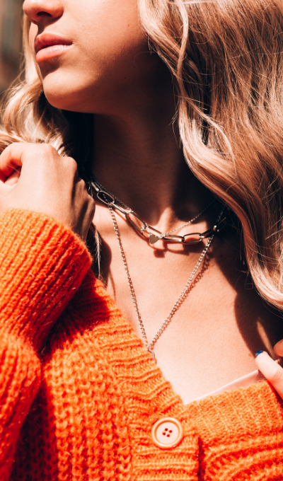 Close-up of a person wearing an orange sweater and layered necklaces.
