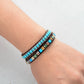 Stacked bracelets with turquoise and brown beads on a wrist against a light gray background