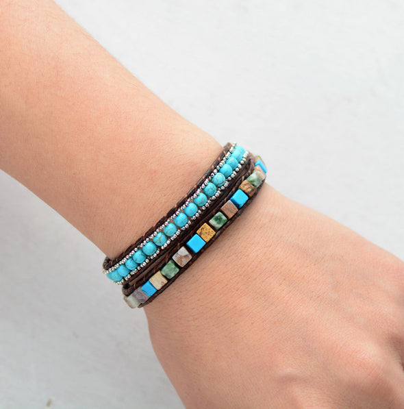 Stacked bracelets with turquoise and brown beads on a wrist against a light gray background