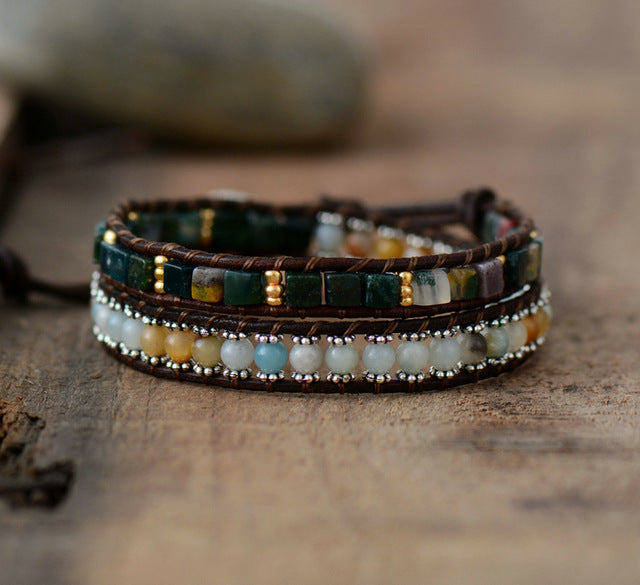 Multistrand beaded bracelet with brown leather wrap on a wooden surface