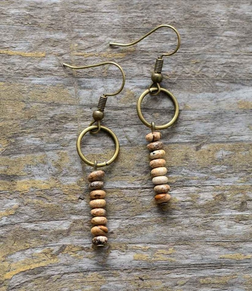 Pair of earrings with circular gold hooks and wooden bead drops on a wooden surface