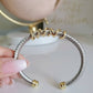 Silver and gold bracelet held by a hand on a light background