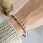 Gold braided bracelet on a wrist with a textured sleeve and blurred background