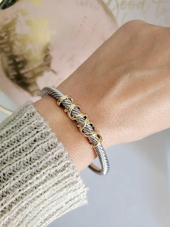Gold braided bracelet on a wrist with a textured sleeve and blurred background