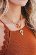 Close-up of a person wearing multiple necklaces with a brown top.
