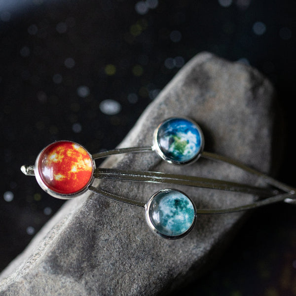 Three planet-themed bangles on a stone surface with a dark background