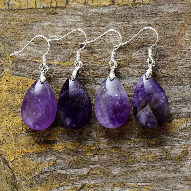 Four purple teardrop earrings on a wooden surface