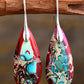 Teardrop-shaped earrings with colorful patterns hanging on a branch.