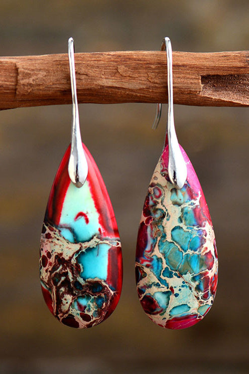 Teardrop-shaped earrings with colorful patterns hanging on a branch.