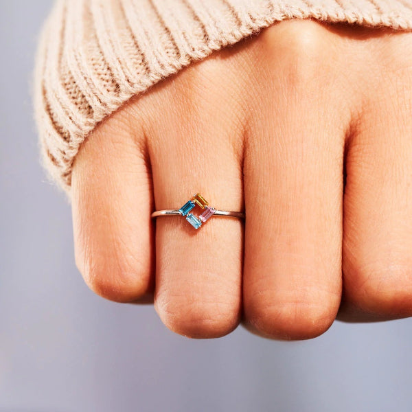 Close-up of a hand wearing a ring with colorful gemstones on a neutral background
