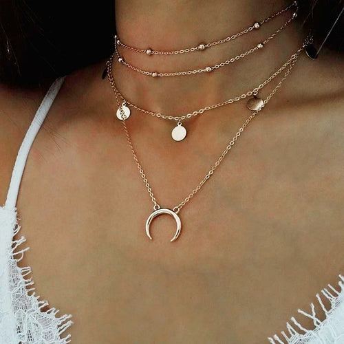 Layered gold necklaces with a crescent moon pendant on a person wearing a white top.
