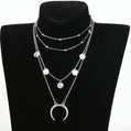 Layered silver necklace with circular pendants on a black mannequin bust.