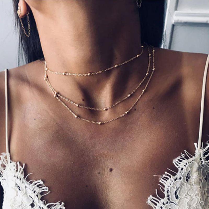 Close-up of a person wearing a delicate gold necklace with a blurred background