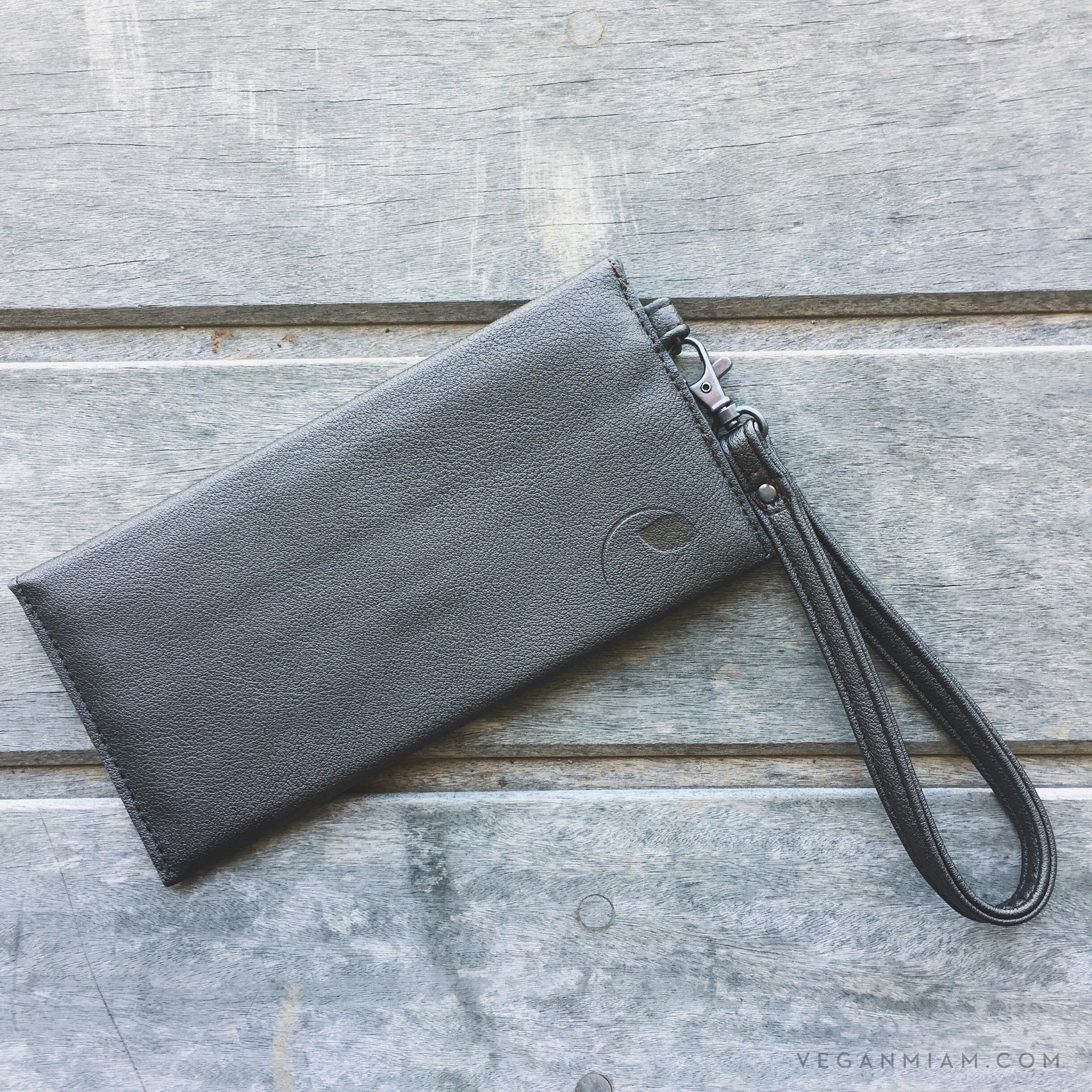 Gray wristlet clutch on a wooden surface with 'veganmian.com' branding.