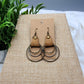 Pair of earrings on a brown card with a plant in the background