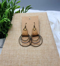 Pair of earrings on a brown card with a plant in the background