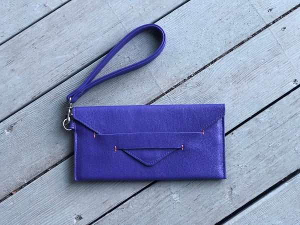 Purple clutch bag with a strap on a wooden surface