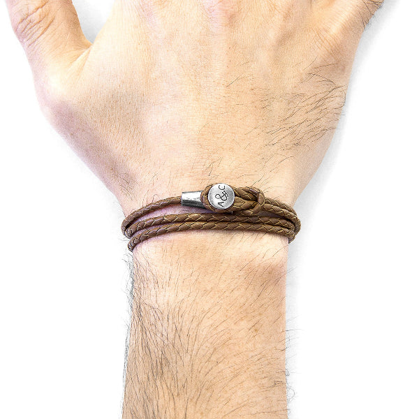 Brown braided bracelet with a silver charm on a wrist against a white background