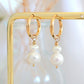 Gold hoop earrings with pearl drops on a gold stand against a soft background