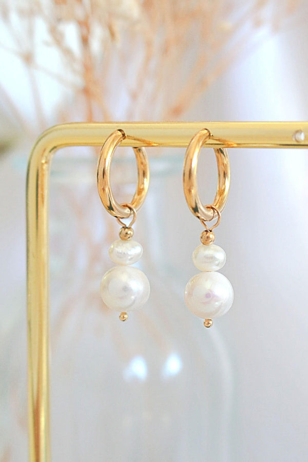 Gold hoop earrings with pearl drops on a gold stand against a soft background